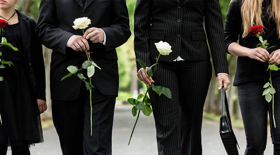 family at funeral service dressed in black and holding single stem roses